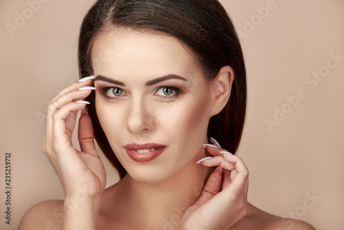 Beautiful woman with clean fresh skin touching face  beige or light brown background