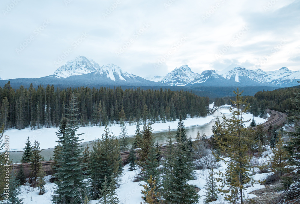 Trains race around a curvy rail road track that snakes alone a frozen river below towering snow capped peaks