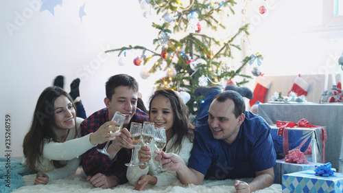 Happy young friends lie on a rug clink glass of champagne during celebrate New Year or Christmas Eve  having great time
