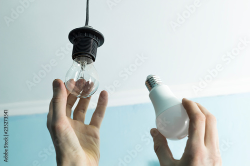Incandescent lamp is changed to LED light by the hands of a man. Energy saving.  photo