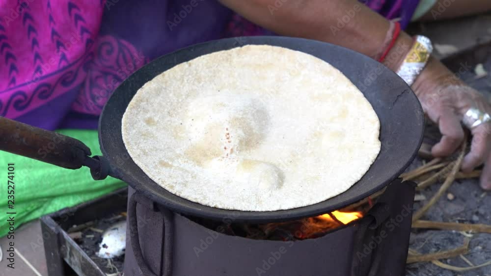 Indian woman cooking traditional indian bread, chapati cooking on open fire in Udaipur, Rajasthan, India. Close up Indian woman cooking traditional indian bread, chapati cooking on open fire in Udaipur, Rajasthan, India. Close up