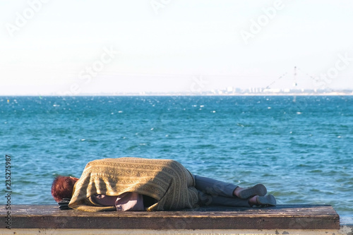 Homeless woman sleeping on a bench on the sea waterfront.
