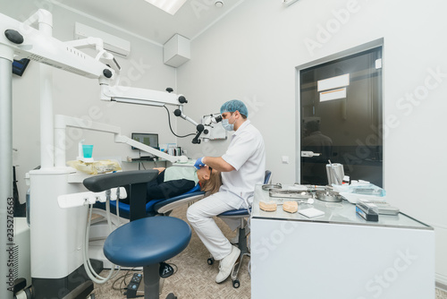 Doctor used microscope. Dentist is treating patient in modern dental office. Operation is carried out using cofferdam. Client is inserted and restored teeth  make denture. Orthodontist and assistant