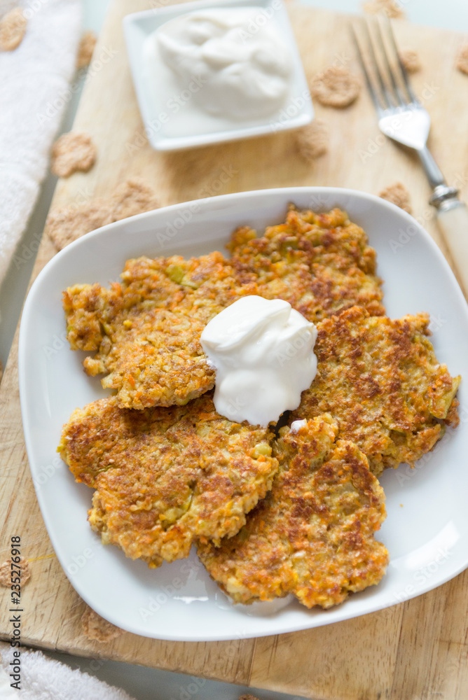 carrot pancakes on a white plate, fork, sour cream on a wooden Board, vegetable vegetarian pancakes carrot pancakes on a white plate, fork, sour cream on a wooden Board, vegetable vegetarian pancakes