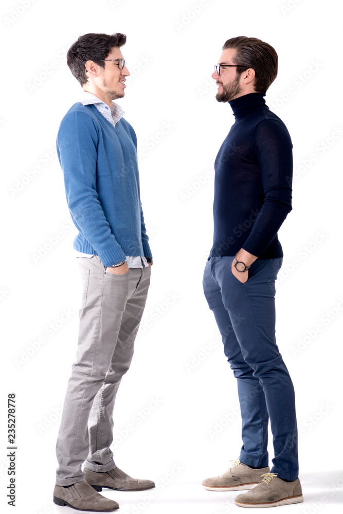 Fototapeta premium Dwóch przystojnych młodych mężczyzn z okularami w stylowych ubraniach, patrząc na siebie z uśmiechem. Pełny strzał studio rysunek, samodzielnie na białym tle