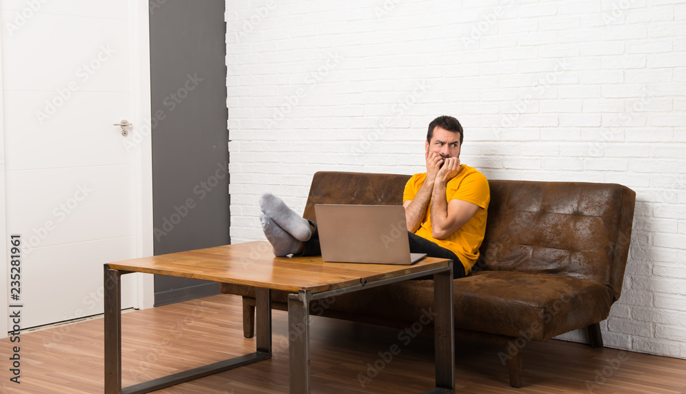 Man with his laptop in a room is a little bit nervous and scared putting hands to mouth
