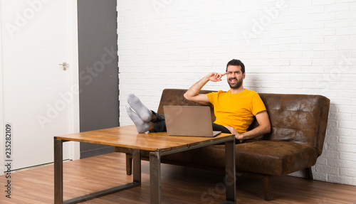 Man with his laptop in a room making the gesture of madness putting finger on the head