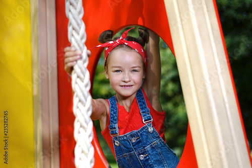 portrait of cute little girl in enim overall and  red T-shirt and  headscarf playing and having fun photo