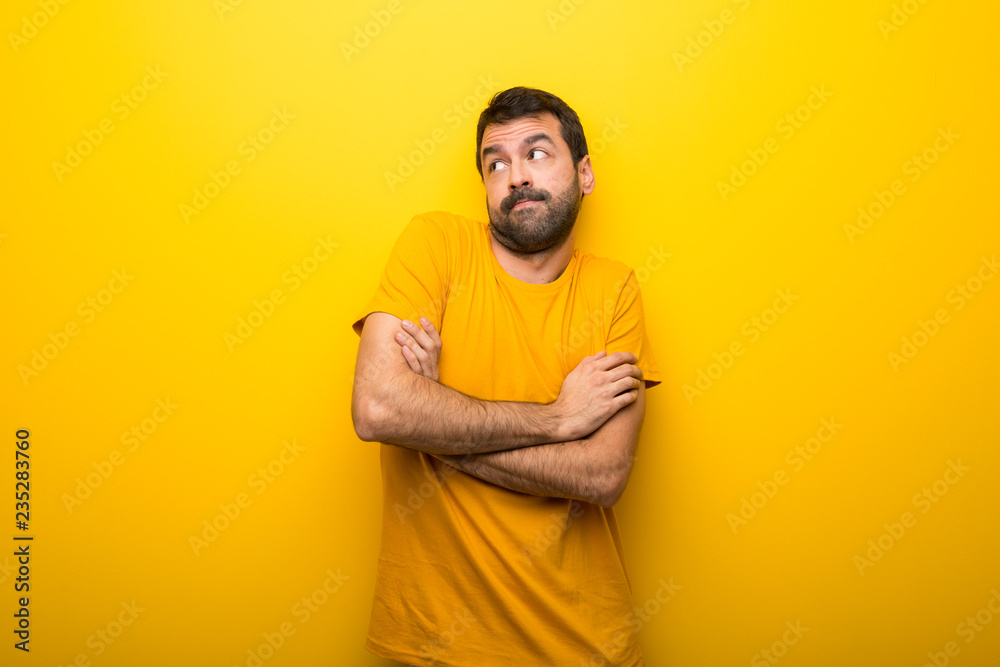 Man on isolated vibrant yellow color making doubts gesture while lifting the shoulders