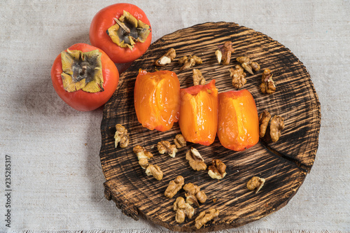 Persimmon fruits in basket and persimmon colored leaves on wooden background, top view.