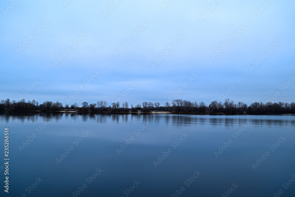 View across the river to the dark forest away in cold weather. View across the river to the dark forest away in cold weather.