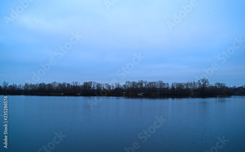 View across the river to the dark forest away in cold weather.