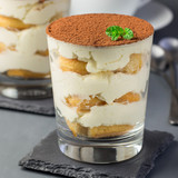 Traditional italian Tiramisu dessert cake in a glass, decorated with cocoa powder and mint, on gray background, square format