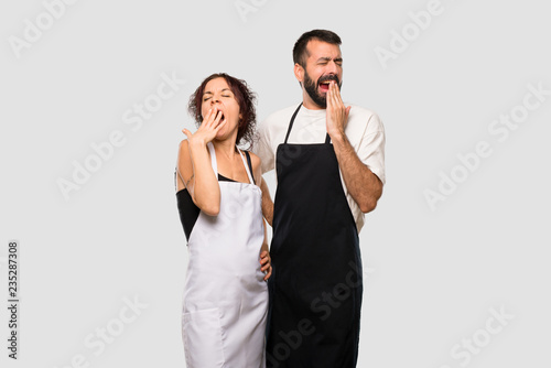 Couple of cooks yawning and covering mouth with hand. Sleepy expression on grey background