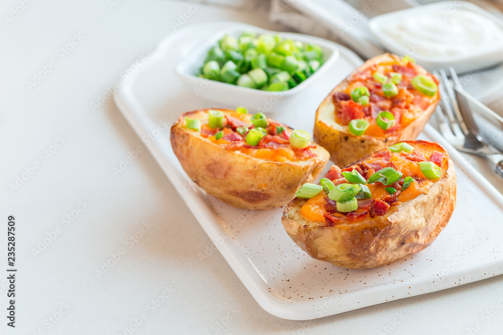 Baked loaded potato skins with cheddar cheese and bacon on ceramic plate, garnished with scallions and sour cream, horizontal, copy space