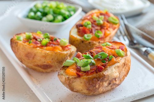 Baked loaded potato skins with cheddar cheese and bacon on ceramic plate, garnished with scallions and sour cream, horizontal