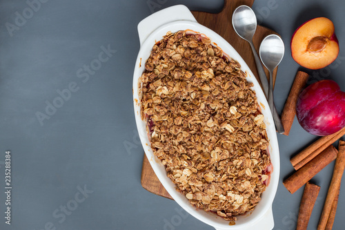Plum crumble pie or plum crisp with oats and spices, in baking dish, top view, horizontal, copy space
