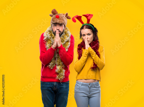 Couple dressed up for the christmas holidays keeps palm together. Person asks for something on yellow background