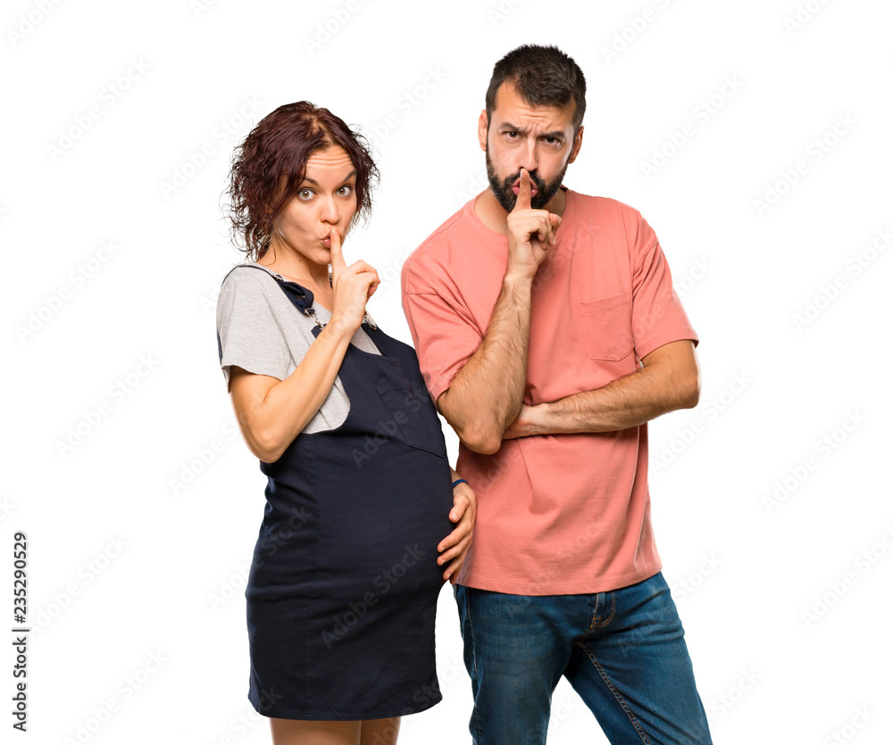 Couple with pregnant woman showing a sign of silence gesture putting finger in mouth on isolated white background Couple with pregnant woman showing a sign of silence gesture putting finger in mouth on isolated white background