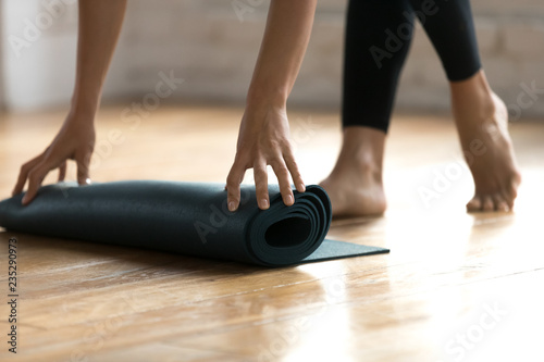 Close up woman hands unrolling mat preparing for fitness workout at gym studio. Sportive female folding rubber carpet after yoga session finishing sport training. Concept of active healthy lifestyle