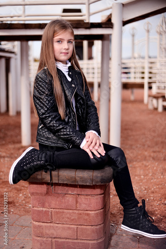 little girl in a black jacket and sneakers sitting on the playground