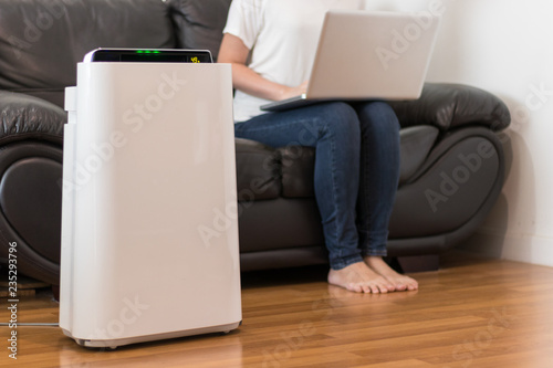 Air purifier in a living room, woman working with laptop with filter for clean room
