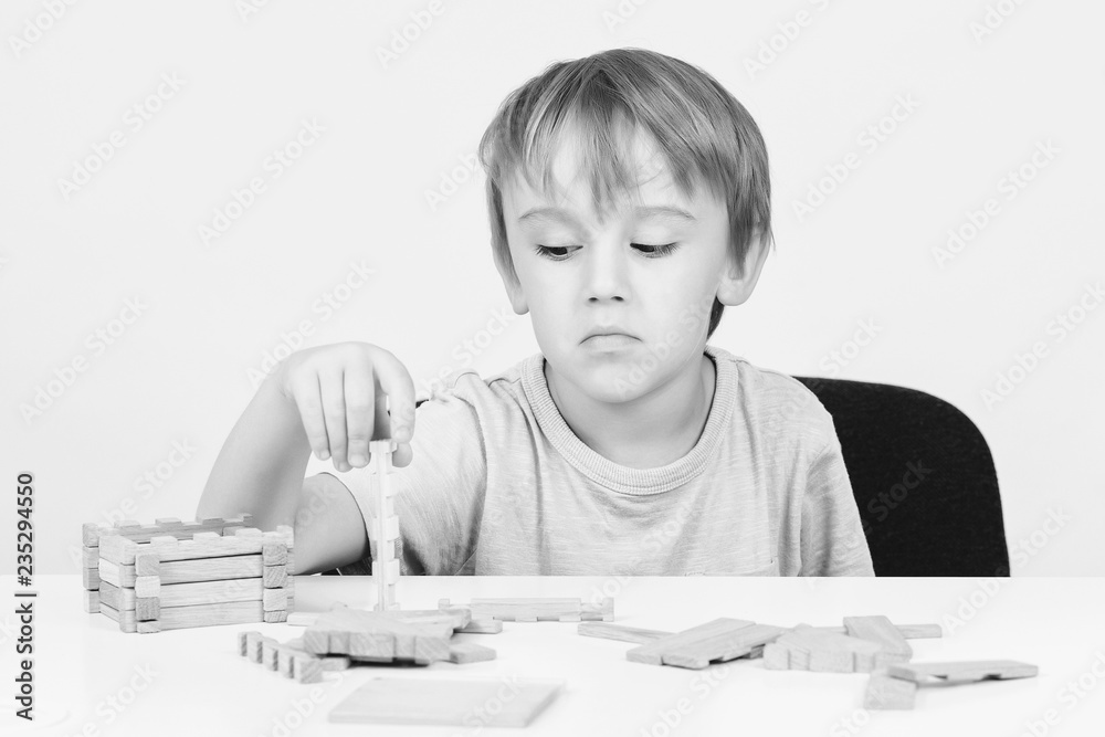 Sad child sitting at table. Child plays with construction toy blocks at the table. Sad bored boy build wooden house. Kid plays with wooden blocks. Sad child playing and dreaming about own home. Sad child sitting at table. Child plays with construction toy blocks at the table. Sad bored boy build wooden house. Kid plays with wooden blocks. Sad child playing and dreaming about own home.