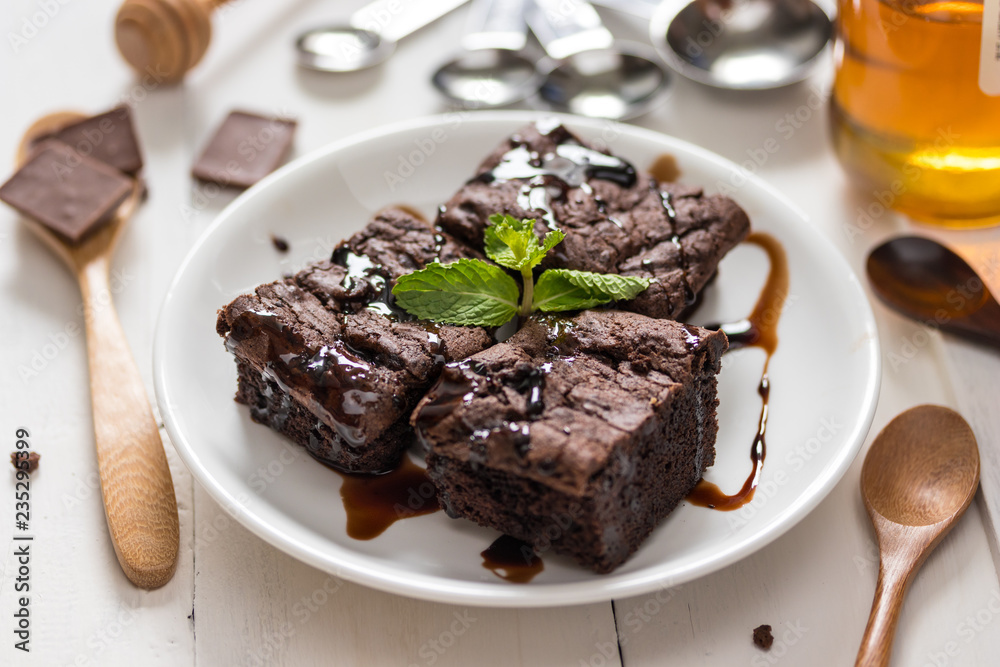 A plate of brownies with chocolate sauce on white wooden background, mint leaf on top, A plate of brownies with chocolate sauce on white wooden background, mint leaf on top,