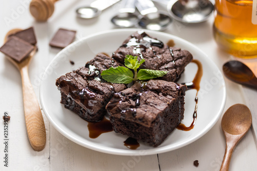 A plate of brownies with chocolate sauce on white wooden background  mint leaf on top 