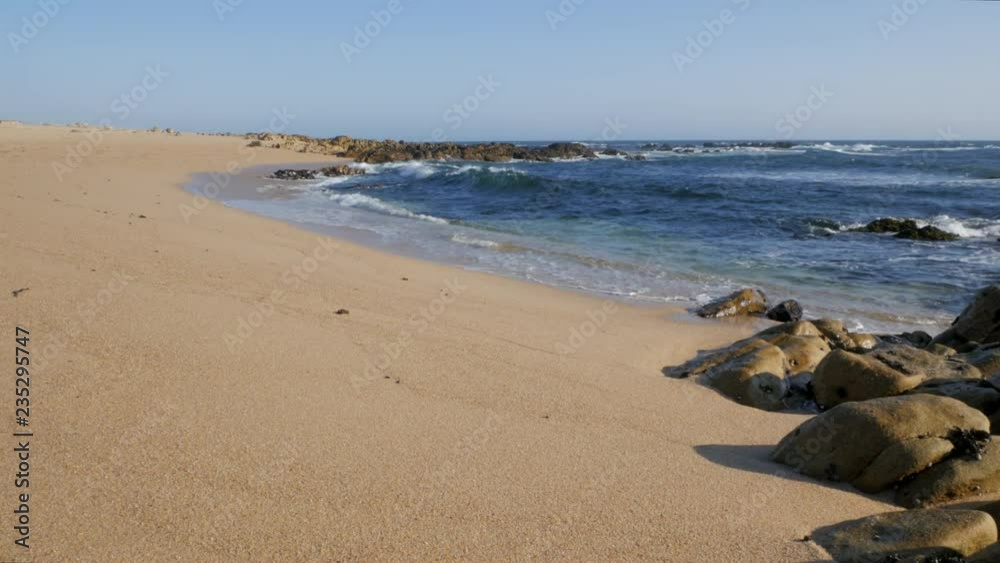 Ocean waves on beach in Porto region, Portugal on a bright sunny day with blue sky and rocks in foreground. Ocean waves on beach in Porto region, Portugal on a bright sunny day with blue sky and rocks in foreground.