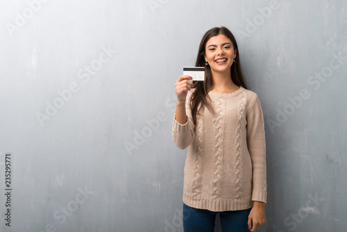 Teenager girl with sweater on a vintage wall holding a credit card