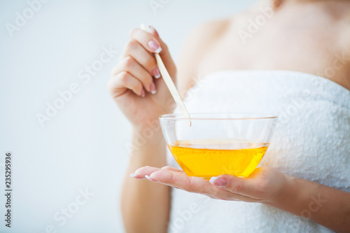 Women hold orange paraffin wax bowl. Woman in beauty salon