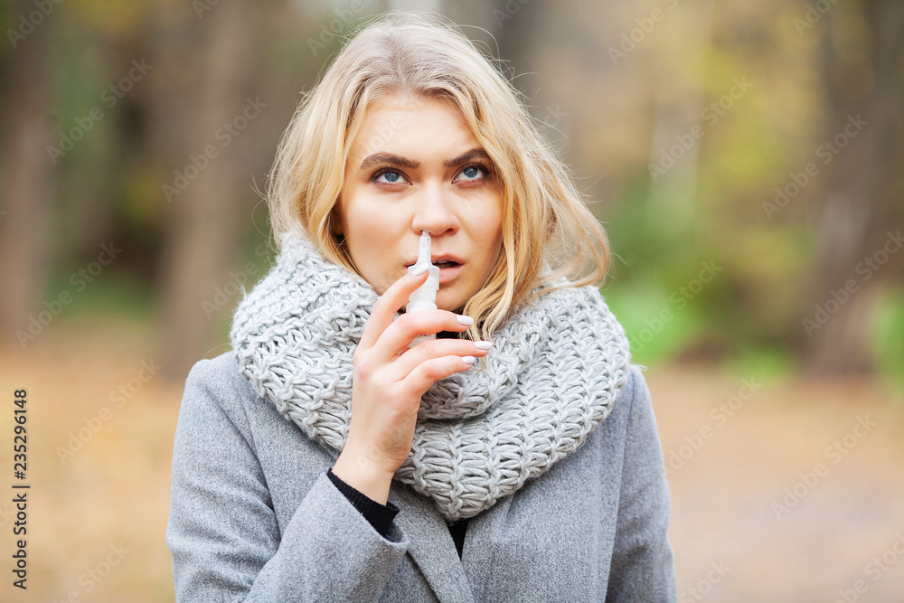 Cold and flu. Young sick woman uses a nose spray at street outside Cold and flu. Young sick woman uses a nose spray at street outside