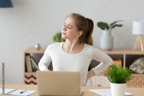 Exhausted girl stretch in chair having spasm working too long in incorrect posture, tired female sit at home desk suffer from back pain, massage trying to relieve symptoms. Sedentary lifestyle concept photo