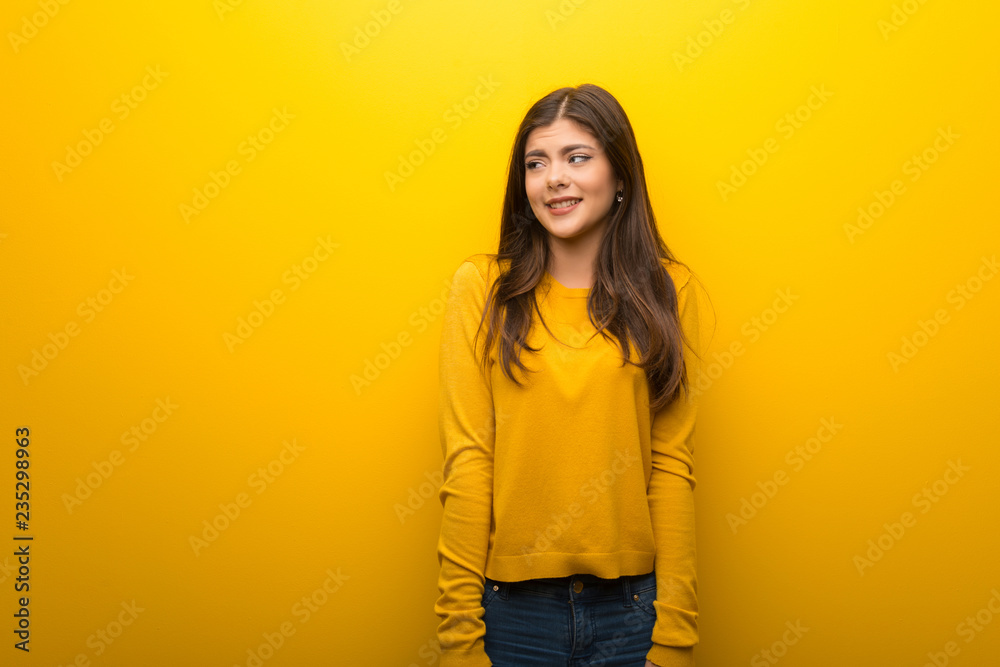 Teenager girl on vibrant yellow background is a little bit nervous and scared pressing the teeth Teenager girl on vibrant yellow background is a little bit nervous and scared pressing the teeth