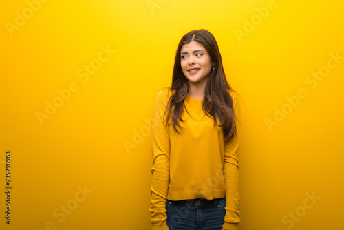 Teenager girl on vibrant yellow background is a little bit nervous and scared pressing the teeth © luismolinero
