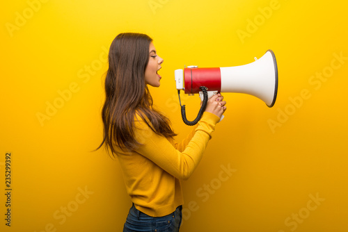 Teenager girl on vibrant yellow background shouting through a megaphone to announce something in lateral position photo