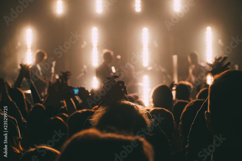 Crowd of people on a rock concert with the hands raised up close up with silhouettes in a stage backlights 