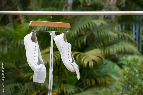 White sneakers hanging on clothesline with hanger in the sun.