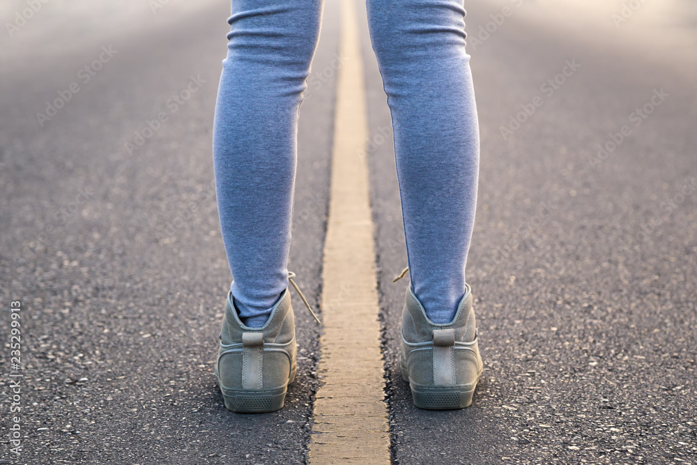 A woman with pair of legs stand astride line road for a exercise in the morning.