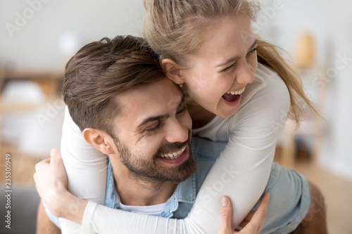 Excited young woman piggyback boyfriend having fun together indoors, millennial couple laughing enjoying spending time together, happy wife hug husband from behind playing funny game at home