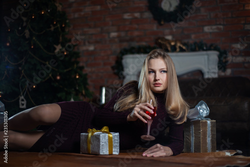 Young woman in a red dress lying on the floor with gifts and champagne near the Christmas tree