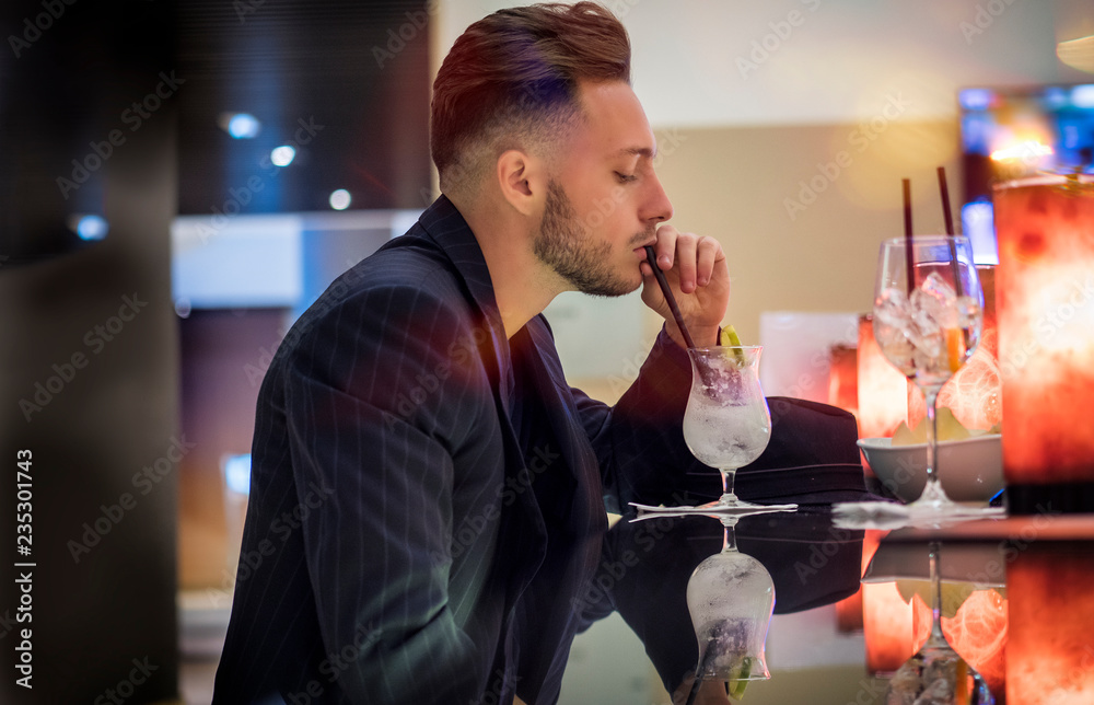 Handsome young man drinking cocktail at bar counter, wearing business ...