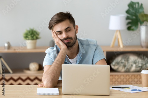 Papier peint Exhausted millennial male hold head with hand sitting at office table falling as