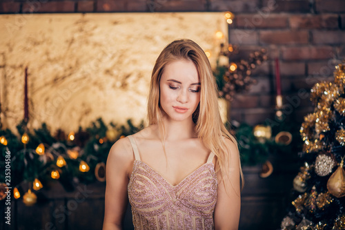 Portrait of luxurious blonde woman in Golden evening dress on Christmas tree and candles background