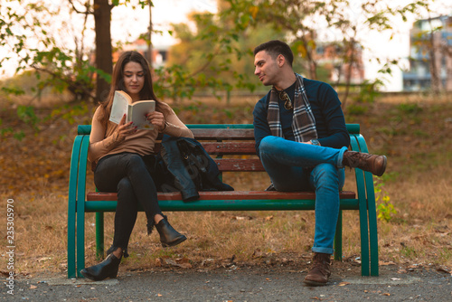 A beautiful girl is reading a book while handsome man is trying to get her attention.