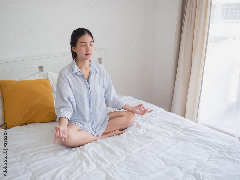 Young asian woman sitting and practicing doing yoga on bed