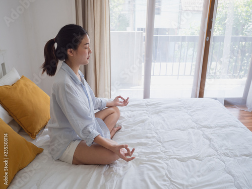 Young asian woman sitting and practicing doing yoga on bed