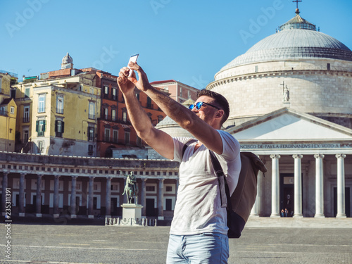 Handsome man with a phone on the background of the square and the old palace in the beautiful city of Naples, Italy. Technology and travel concept