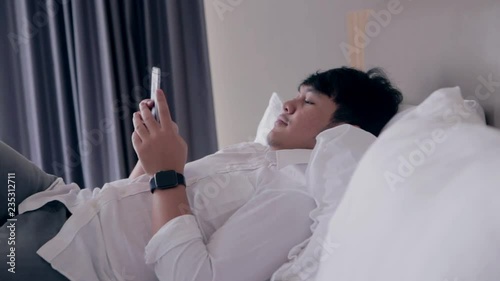 Young asian handsome man using smartphone laying down on bed while chatting with friend